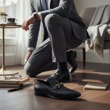 ARQS.PK black leather formal loafers with metallic horsebit detail worn by a man in a grey suit in a bright office.
