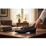 ARQS.PK black leather tassel loafer dress shoe held on a wooden desk in a professional office setting