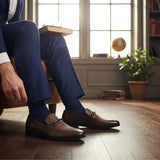 ARQS.PK brown leather horsebit loafers with textured vamp detail worn by a man in a blue suit in a study setting